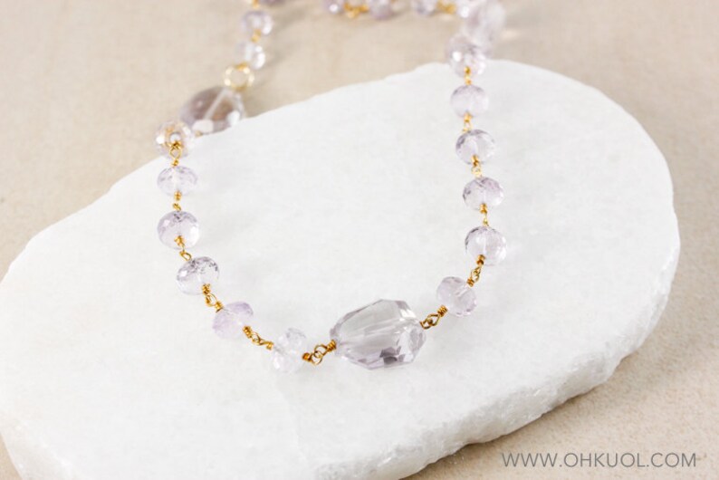 May include: A delicate gold chain necklace with light purple faceted beads and a larger, faceted, light purple gemstone pendant.