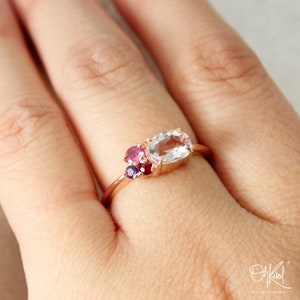 May include: A rose gold ring with a large oval-shaped clear gemstone and smaller pink and purple gemstones.