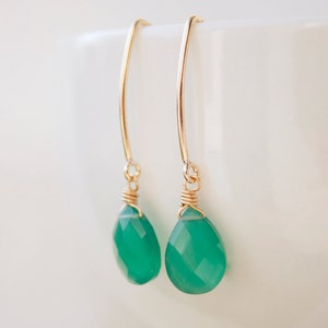 May include: A pair of gold earrings with green gemstone drops. The earrings are made with a simple wire design and feature a teardrop-shaped gemstone.