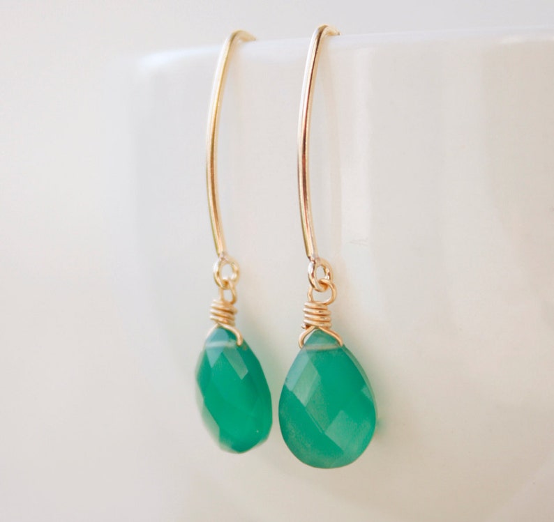 May include: A pair of gold earrings with green gemstone drops. The earrings are made with a simple wire design and feature a teardrop-shaped gemstone.