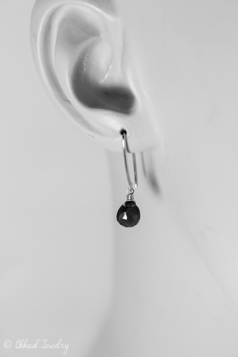 Pode incluir: Um par de brincos de prata com uma gota de pedra preciosa preta.
