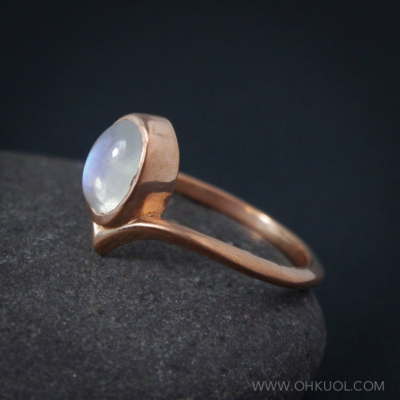 Puede incluir: Un anillo de oro rosa con una piedra de luna blanca engastada en un dise&ntilde;o simple y elegante.