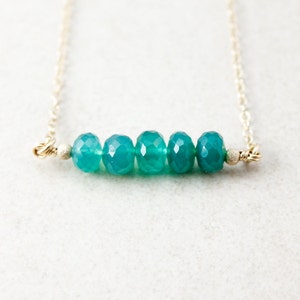 May include: A delicate gold chain necklace with a row of five faceted teal green gemstones.