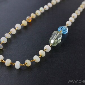 May include: A gold chain necklace with white opal beads and a green and blue crystal pendant.