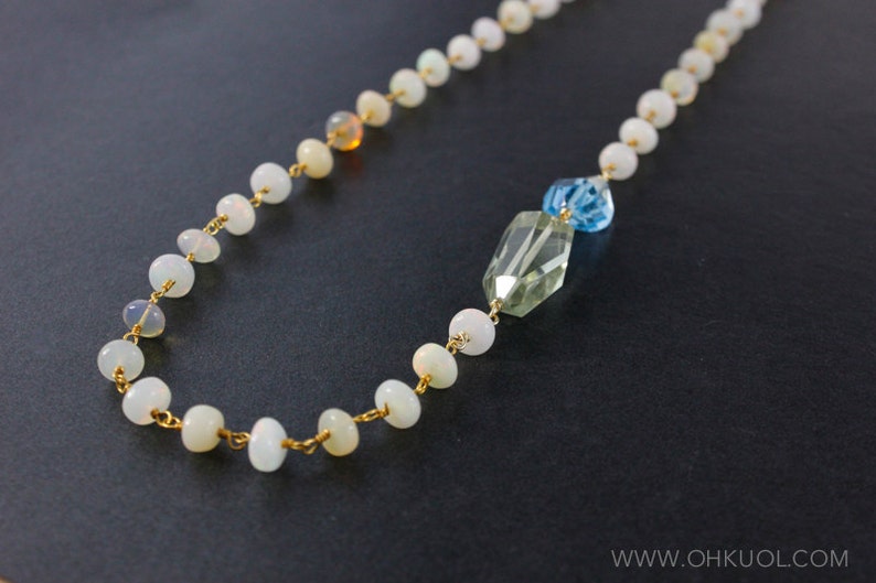 May include: A gold chain necklace with white opal beads and a green and blue crystal pendant.