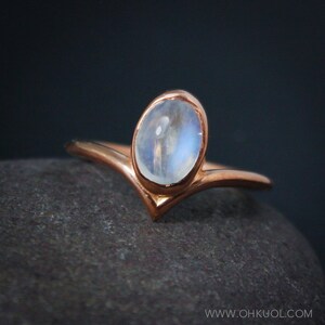 Puede incluir: Un delicado anillo de oro rosa con una banda en forma de V y una piedra de luna redonda.