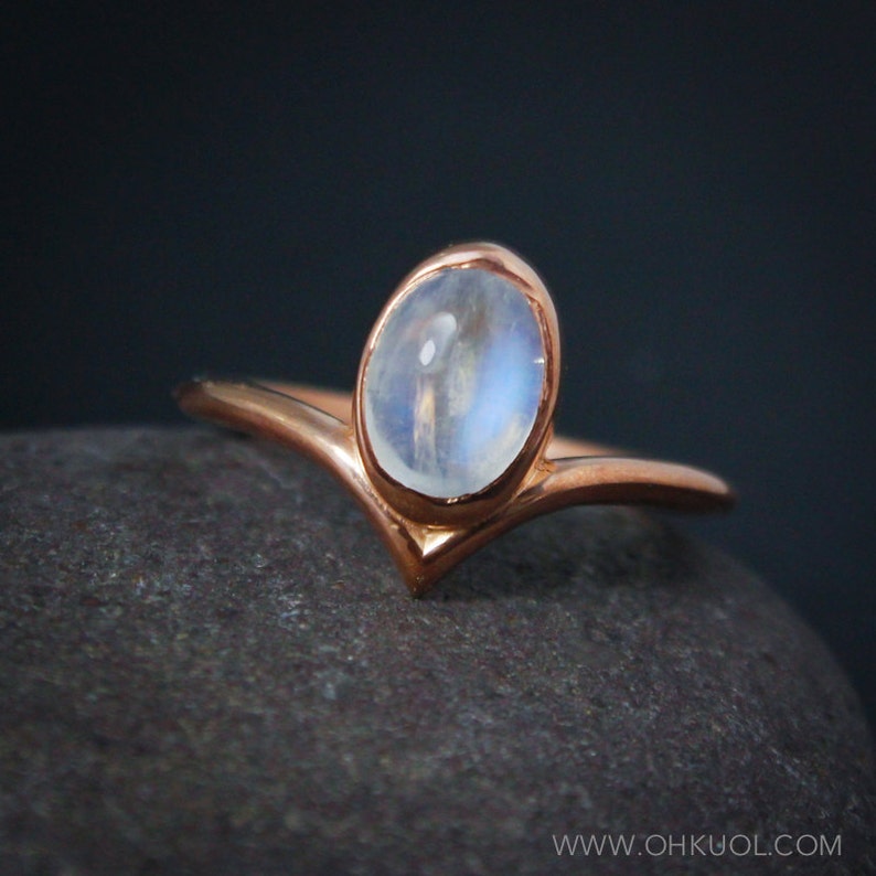 Puede incluir: Un delicado anillo de oro rosa con una banda en forma de V y una piedra de luna redonda.