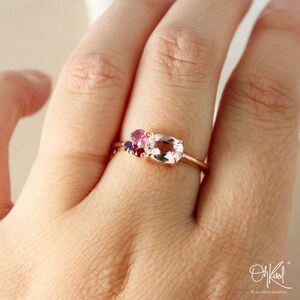May include: A rose gold ring with a large oval-shaped clear gemstone and smaller pink and purple gemstones.