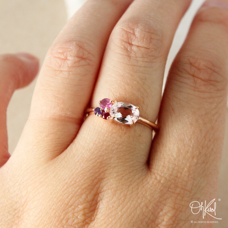 May include: A rose gold ring with a large oval-shaped clear gemstone and smaller pink and purple gemstones.