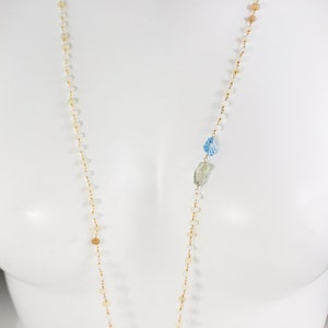 May include: A long gold chain necklace with small white and brown beads and two larger blue and green gemstone accents.