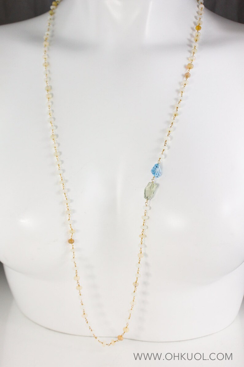 May include: A long gold chain necklace with small white and brown beads and two larger blue and green gemstone accents.