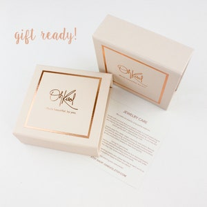 May include: A gift box with a rose gold logo that says "OhKool made beautiful by you." The box is closed and ready for gifting. The box is sitting on a white surface. The text "gift ready!" is written in cursive above the box.
