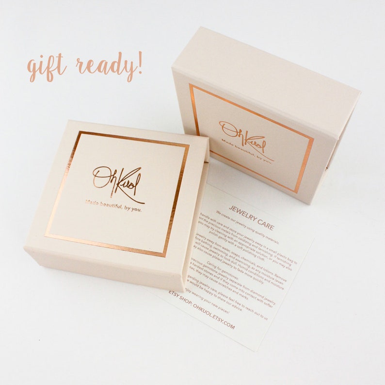 May include: A gift box with a rose gold logo that says "OhKool made beautiful by you." The box is closed and ready for gifting. The box is sitting on a white surface. The text "gift ready!" is written in cursive above the box.