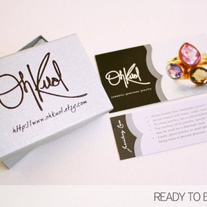 May include: A silver jewelry box with a white lid and the text "On Kool" and "http://www.okkuol.etsy.com" printed on it. The box is open and a gold chain is visible inside. There are two cards with the text "On Kool" and "Romantic Gemstone Jewelry" on them. One card has a close-up image of a ring with three gemstones.