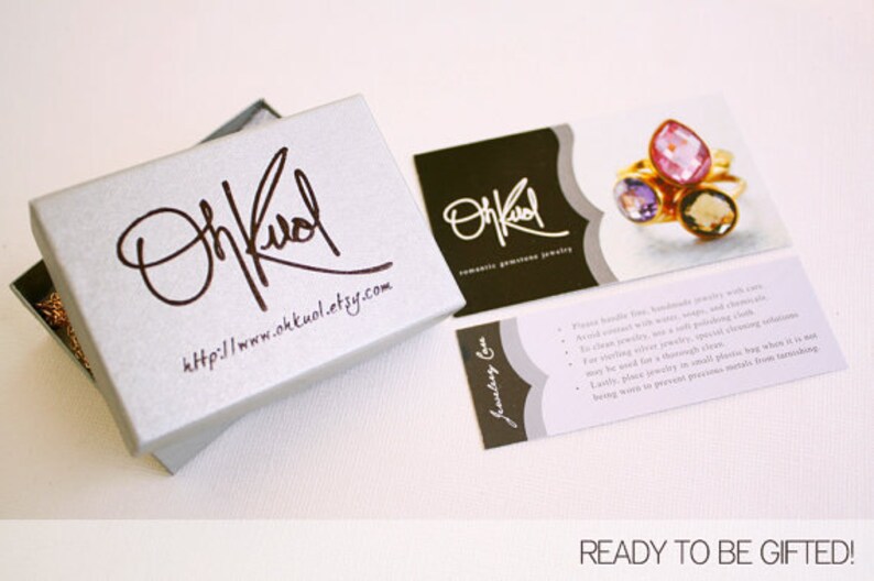 May include: A silver jewelry box with a white lid and the text "On Kool" and "http://www.okkuol.etsy.com" printed on it. The box is open and a gold chain is visible inside. There are two cards with the text "On Kool" and "Romantic Gemstone Jewelry" on them. One card has a close-up image of a ring with three gemstones.