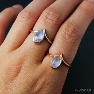 Puede incluir: Dos anillos de plata con piedras de luna. Los anillos est&aacute;n en el dedo de una persona. Ambos anillos tienen forma de V.