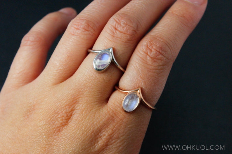 Puede incluir: Dos anillos de plata con piedras de luna. Los anillos est&aacute;n en el dedo de una persona. Ambos anillos tienen forma de V.