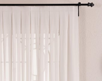 Pode incluir: Um painel de cortina branco sólido com pregas verticais ao longo da borda superior, suspenso por um varão de cortina de metal preto fino com um remate decorativo na extremidade. O tecido cai em dobras retas e uniformes, permitindo luz.