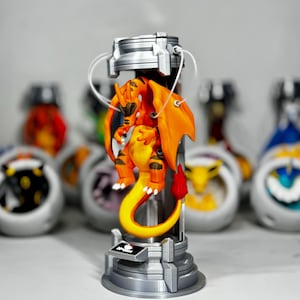 May include: An orange and yellow dragon-like creature with wings and a flame-tipped tail is suspended inside a silver cylindrical containment chamber. The base features a small black plaque with the text No. 0006 printed in white.