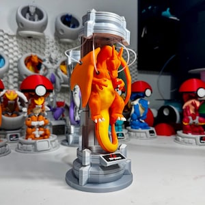 May include: An orange dragon-like creature figure suspended inside a gray cylindrical containment chamber. The figure has wings, a long tail, and white claws. A small black plaque at the base of the chamber displays the text No. 0006 in white.
