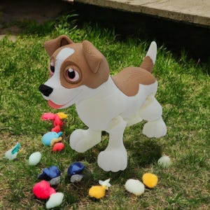 May include: A white, brown, and tan toy dog with large eyes and a black nose stands on green grass. Colorful toy eggs and other toys are scattered around the dog. The dog has a friendly expression.