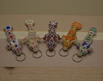 Pode incluir: Cinco chaveiros em forma de dragão com designs intrincados. Cada chaveiro apresenta um esquema de cores diferente, incluindo vermelho, branco, azul, castanho, laranja e verde. Os chaveiros são feitos de um material flexível e têm um porta-chaves prateado.