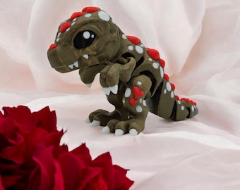 May include: A small, brown, articulated dinosaur toy with red hearts and white spots. The dinosaur has large, black eyes and a toothy grin.
