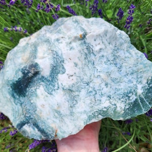 May include: A large, irregular slab of moss agate featuring a white base with intricate, branching dark green and teal inclusions that resemble organic, fern-like patterns throughout the stone's textured, semi-translucent surface.