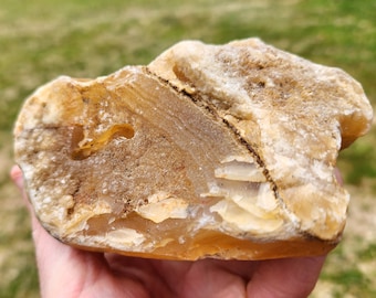 May include: A natural, raw stone with a mix of tan, beige, and white colors. The stone has a rough, textured surface with a visible fracture line. The overall shape is irregular, showcasing the stone's natural form. The stone is a unique decorative item.