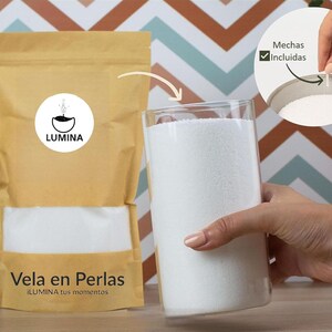 Puede incluir: Un cilindro de vidrio transparente lleno de perlas de vela blancas, sostenido por una mano. Una bolsa de papel marrón con una ventana transparente y el texto "Vela en Perlas" está al lado.