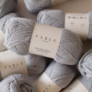 May include: A close-up of a skein of light grey yarn labelled "FABLE handknit Pure Baby Alpaca 100% Baby Alpaca 500g".