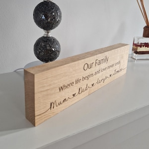 May include: A wooden sign with the text "Our Family Where life begins and love never ends Mum Dad Lary's Tomos" engraved on it. The sign is light brown and has a natural wood grain.