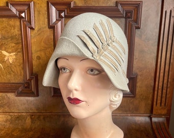 1920s delightful dove-grey felt cloche unworn with asymmetrical shape and military velvet ribbon. New Old Stock, 21" small