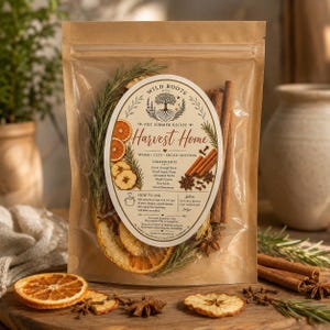 Op de afbeelding: Een doorzichtige plastic zak met een sudderrecept voor op het fornuis genaamd Harvest Home van Wild Roots & Co. De inhoud bestaat uit gedroogde sinaasappelschijfjes, appelschijfjes, kaneelstokjes, steranijs, kruidnagels en gedroogde rozemarijn.