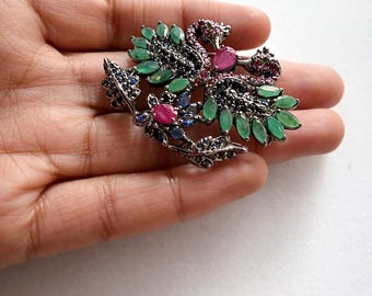 Puede incluir: Broche de pavo real plateado con piedras preciosas verdes, rosas y azules. El broche presenta un diseño detallado de un pavo real con las plumas extendidas. Las piedras preciosas son esmeraldas, rubíes y zafiros, que añaden color y brillo.