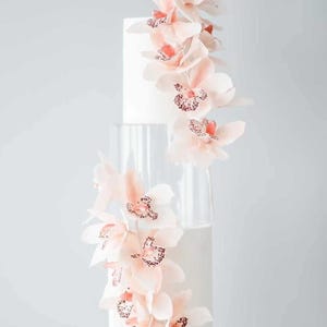 Peut inclure: Un gâteau de mariage blanc à quatre étages décoré d'orchidées roses en cascade. Le gâteau est sur un support à gâteau blanc.