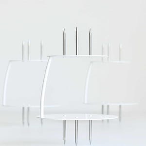 Może przedstawiać: Biały metalowy stojak na ciasto z pięcioma metalowymi kolcami. Stojak jest zaprojektowany do trzymania ciasta lub innego deseru.