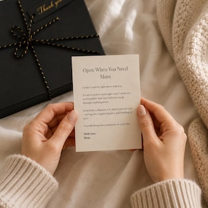 May include: A black gift box tied with gold and black twine, with a "Thank you" tag. A card that reads "Open When You Need Mom" is held in front of the box. The card contains a message from Mom.