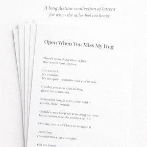 May include: A stack of white paper cards with printed text. The top card reads "Open When You Miss Me" and "Open When You Miss My Hug." The cards contain sentimental messages about missing someone and the comfort of a hug.