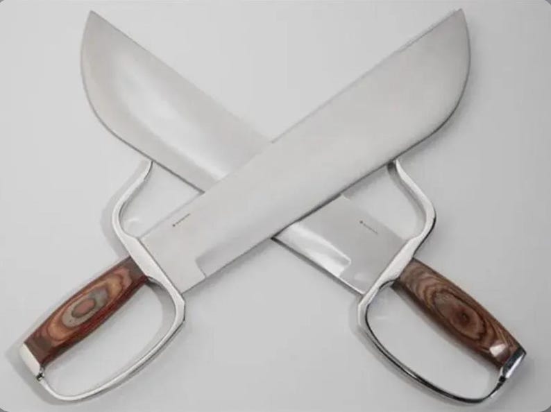 May include: Two crossed, large, silver-bladed knives with wooden handles. The blades are wide and curved, and the handles feature a finger guard. The knives are displayed against a white background.