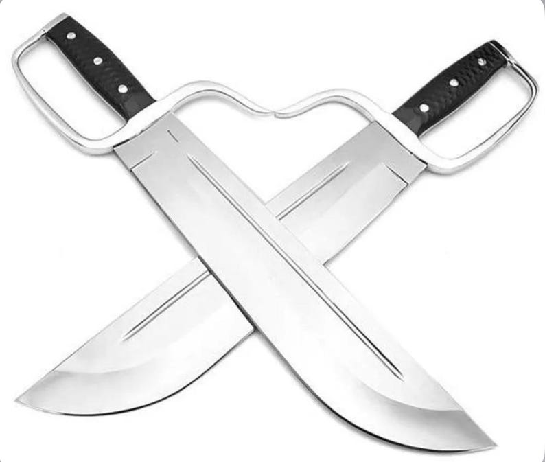 May include: Two crossed silver metal butterfly swords with black handles. The blades are wide and curved, with a sharp edge. The handles have a finger loop for grip.