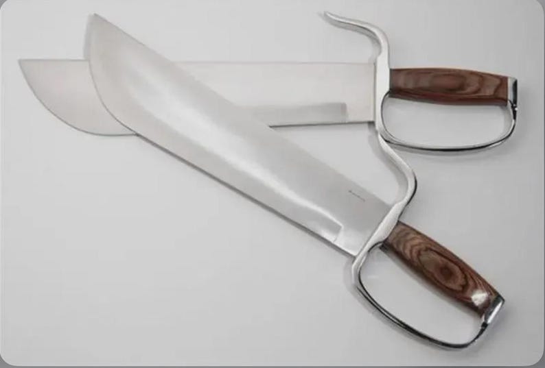 May include: Two stainless steel butterfly swords with wooden handles. The blades are wide and curved, with a polished finish. The handles have a finger loop design.