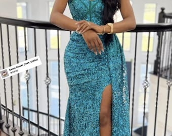 May include: A woman wearing a teal sequined halter dress with a thigh-high slit. The dress has a criss-cross design at the neckline. The woman is standing on a staircase with a black railing. The text "Come Closer (feat. Drake) WizKid" is visible in the image.