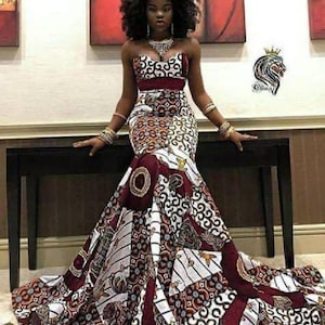 May include: A woman wearing a strapless, fitted, mermaid-style dress with a colorful African print pattern. The dress has a burgundy waistband and a white, red, and gold print.