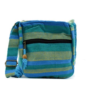 May include: A crossbody bag featuring horizontal stripes in shades of teal, blue, and yellow. The bag includes a black zippered front pocket with a fabric pull tab adorned with a small wooden bead and an adjustable shoulder strap with metal hardware.