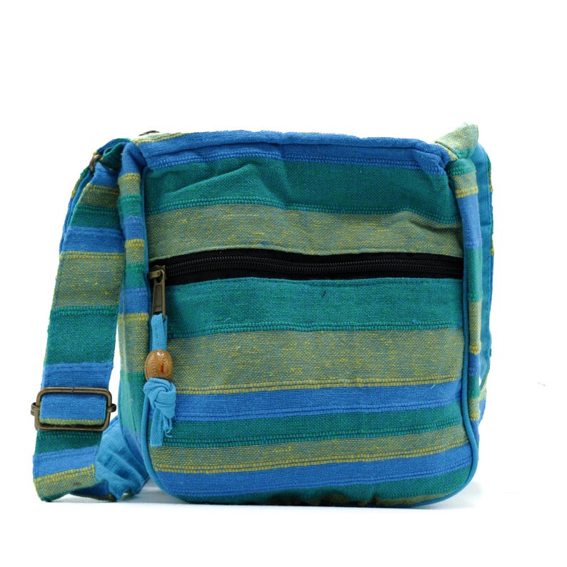 May include: A crossbody bag featuring horizontal stripes in shades of teal, blue, and yellow. The bag includes a black zippered front pocket with a fabric pull tab adorned with a small wooden bead and an adjustable shoulder strap with metal hardware.