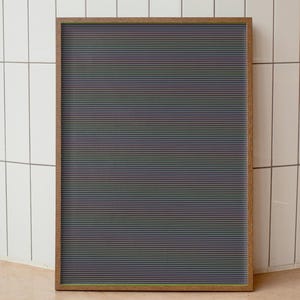 May include: A framed, rectangular letter board with a dark gray background and horizontal lines in various colors. The frame is made of wood. The board is displayed against a white tiled wall.