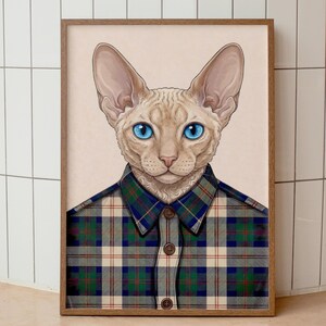 May include: A framed art print featuring a Sphynx cat with striking blue eyes, wearing a plaid shirt in shades of green, blue, and beige. The cat's fur is a light tan color, and the artwork is set against a neutral background.