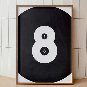 May include: A framed print featuring a large black and white graphic of the number eight, resembling a billiard ball. The number eight is composed of two white circles with the number eight in the center of each. The frame is a warm brown color.