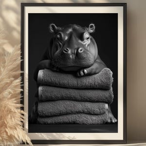 Pode incluir: Uma fotografia a preto e branco de um hipopótamo a descansar sobre uma pilha de toalhas cinzentas. O hipopótamo está a olhar para a câmara com uma expressão cansada.